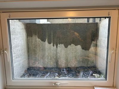 Fotografi av et vindu som ser ut på en betongkonstruksjon (kanskje en kjeller eller grunntank) med synlig fuktighetsskade.