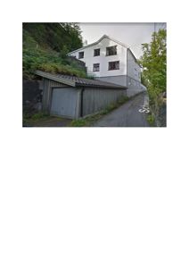 Fotografi av en hvit bygning med etasjer og vinduer, sett fra en vei med en garasje i forgrunnen.