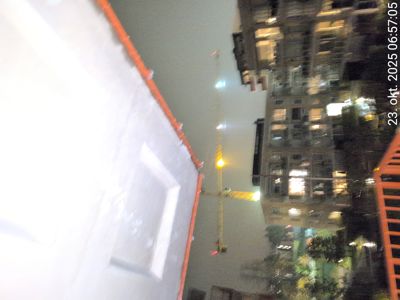 Fotografi tatt fra en byggeplass eller balkong som viser en gule kran, en bygning i bakgrunnen og en del av en fasade i forgrunnen.