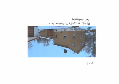 Fotografi av en eksisterende bygning (hus) sett fra siden, med snø på bakken og trær i bakgrunnen.