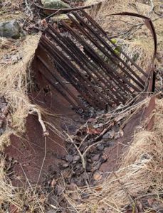 Fotografi av rustet metallskrot, muligens en del av en gammel konstruksjon eller gjenstand, liggende i urørt natur.