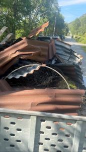 Fotografi av en haug med skrotet takplater (både rustfrie og rustete) og gjerde som ligger i en container eller på bakken.