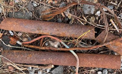 Fotografi av rustne metallrør og kabler liggende på bakken.
