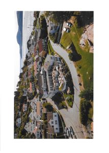 Fotografi av en kystby eller tettsted sett fra luften, med hus, veier, vann og fjell.