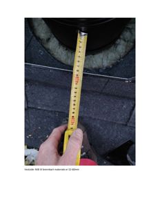 Fotografi som viser en hånd som holder en målebånd for å måle avstanden til brennbart materiale på en vestside av en bygning.