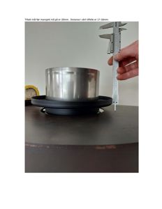 Fotografi av en metallisk komponent (manskjett) på en overflate, målt med en skruemåler. Bildet illustrerer en fysisk måling eller kontroll av et produkt.