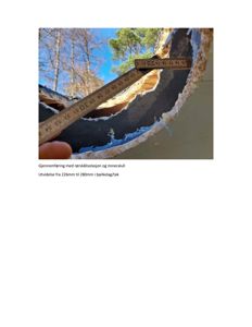 Fotografi som viser en gjennomføring av rørskålisolasjon og mineralull i bjelkelag/tak, med en målebånd som viser dimensjonen.