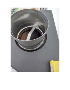 Fotografi av en metallisk ventilasjonsrør eller utløp som er montert i en flate, sannsynligvis under et tak eller i en teknisk rom.