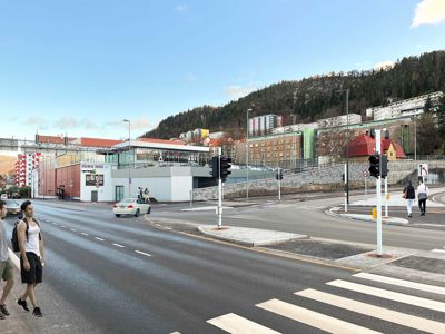 Fotografi av en gatetomme med trafikk, fotgjengere og bygninger i bakgrunnen.