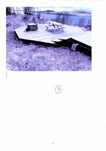 Fotografi av en uteplass med en terrasse, et bord og en kasse, med utsikt over vann og fjell.