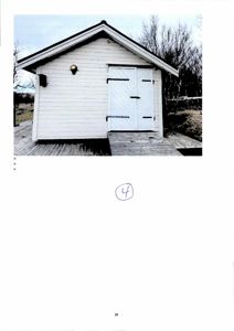 Fotografi av en hvit, liten bygning (kanskje uthus eller garasje) sett fra front.