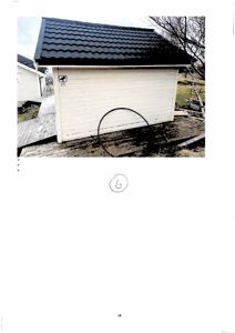 Fotografi av en hvit garasje med svart tak sett fra siden.