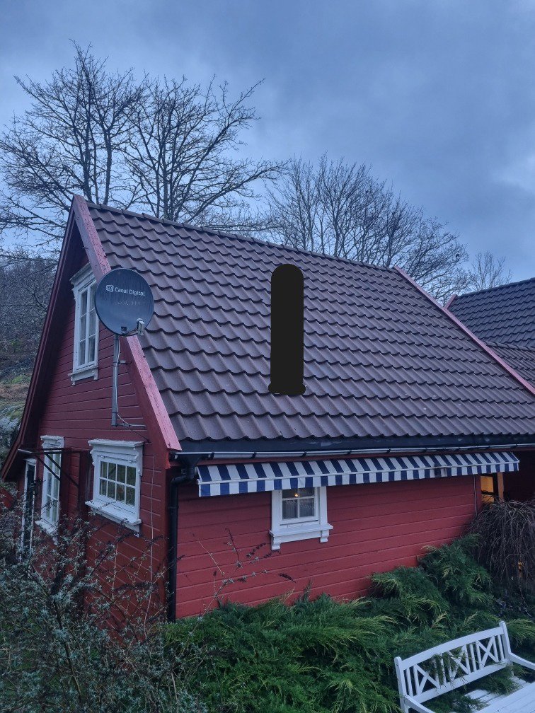 Fotografi av en rød hytte med hvite vinduer, et tak med mørke fliser og en blå-hvit markise.