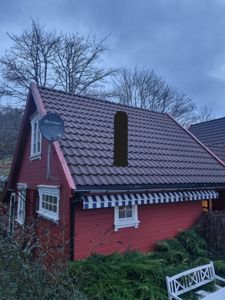 Fotografi av en rød hytte med hvite vinduer, et tak med mørke fliser og en blå-hvit markise.