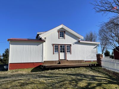 Fotografi av en hvit, trepanelt bygning med rød takkant og en liten veranda foran, sett fra en vinkel.
