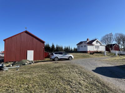 Fotografi av en eiendom med et stort rødt skur, en hvit hus og en bil parkert på en grusvei.