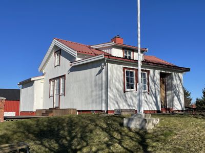 Fotografi av en hvit, trepanelert bygning med rødt tak og vinduer mot en blå himmel.