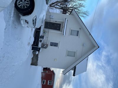 Fotografi av en hvit, toetasjes villa med snødekke, sett fra foran med en bil i forgrunnen.