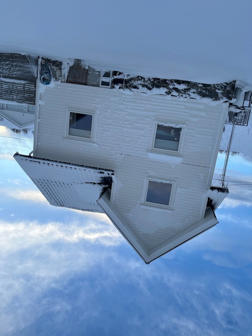 Fotografi av en hvit, toetasjes bolig med snø på tak og bakke, sett fra en skrå vinkel.