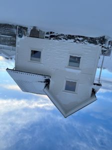Fotografi av en hvit, toetasjes bolig med snø på tak og bakke, sett fra en skrå vinkel.