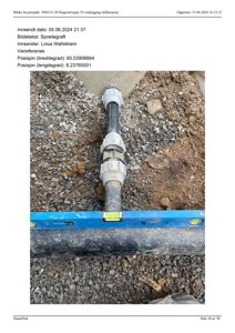 Fotografi av en svart plastrørledning (spredegrøft) som ligger i grus under jorden, med en blå vannivålinje på toppen.