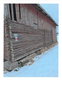 Fotografi av en gammel, rød og grå tømmerbygning (sannsynligvis et uthus eller skur) sett fra siden. Bygningen står på steinfundament i snø.