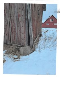 Fotografi av en gammel, rød trebygning i snø, med en annen rød bygning i bakgrunnen.