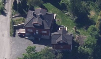 Luftfoto av en tomt med to røde hus, en vei og omgivende natur.