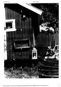 Fotografi av en mørk trebygning sett fra siden, med et vindu, en utvendig boks og en gressklipper i forgrunnen.