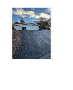 Fotografi av en hvit garasje med to dører og to søppelcontainere foran, sett fra en asfaltert kjørevei.