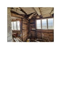 Fotografi av et gammelt, delvis nedrøvet trehus med skadet takkonstruksjon og utstyrte vinduer.
