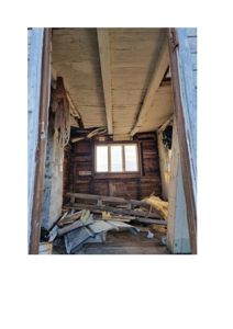 Fotografi av et gammelt, forlatt rom med skadet tak og gulv, sett innad gjennom en døråpning.