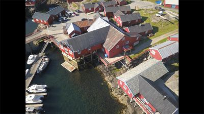 Luftfoto av en gruppe røde bygninger langs en vannkant, inkludert båter og en kai.