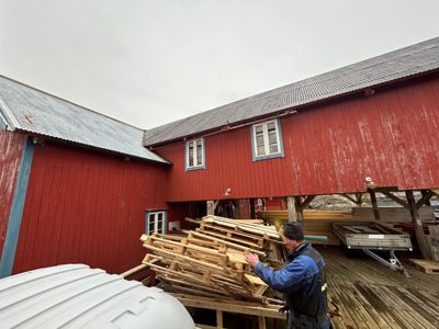 Fotografi av en rød bygning med en mann som arbeider med treverk i forgrunnen.
