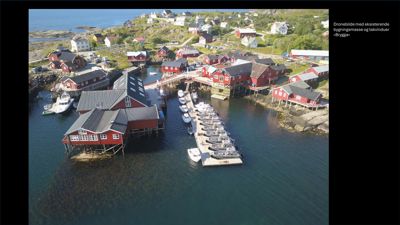 Et dronelagte fotografi av et havneområde med røde hytter, båter og en kai.