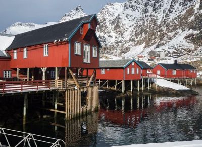 Fotografi av røde stuer på stoler i en fjord med snødekte fjell i bakgrunnen.