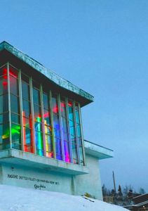 Fotografi av en bygning med fargede lys i vinduene, sett fra et lavt vinkel mot en snødekt bakke.