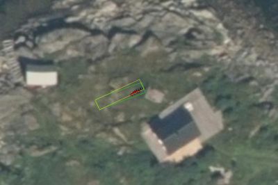 Flyfoto eller satellittbilde av et område med flere bygninger, der en grønn rektangelmarkering (tomtegrense) er tegnet over en av dem.