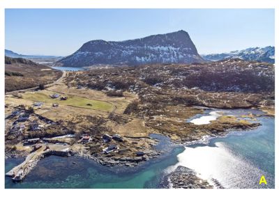 Luftfoto av et kystlandskap med fjell, vann og spredt bebyggelse.