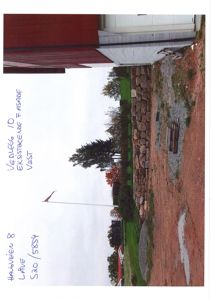 Fotografi av en eksisterende fasade (vest) med en steinmur og et hus i bakgrunnen.