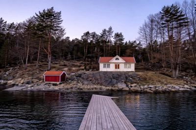 Fotografi av en hvit hytte og en mindre utedekk ved vannet, sett fra en kai.