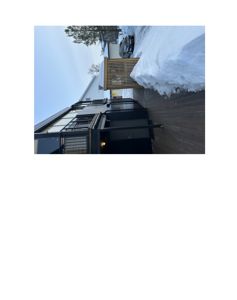 Fotografi av en moderne boligfasade sett fra siden, med snø i bakgrunnen og et bilparkert.