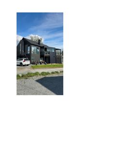 Fotografi av en moderne, mørk farget bolig under eller etter ferdigstillelse, med bil og grusvei i forgrunnen.