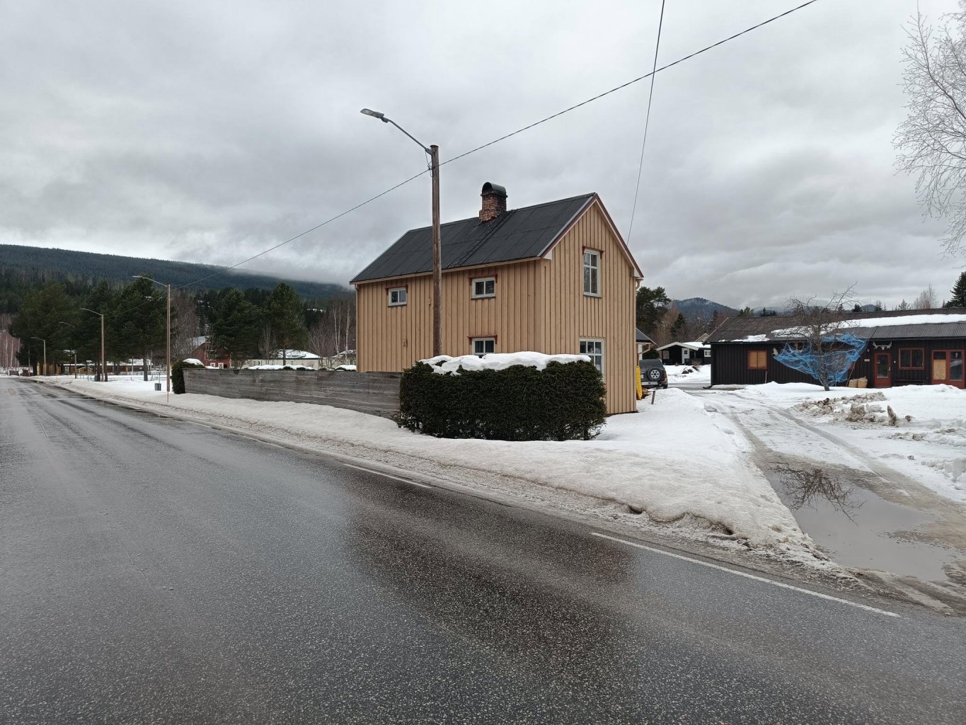 Fotografi av en eksisterende bygning (hus) sett fra veien i et snøklødd landskap.