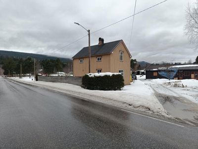 Fotografi av en eksisterende bygning (hus) sett fra veien i et snøklødd landskap.