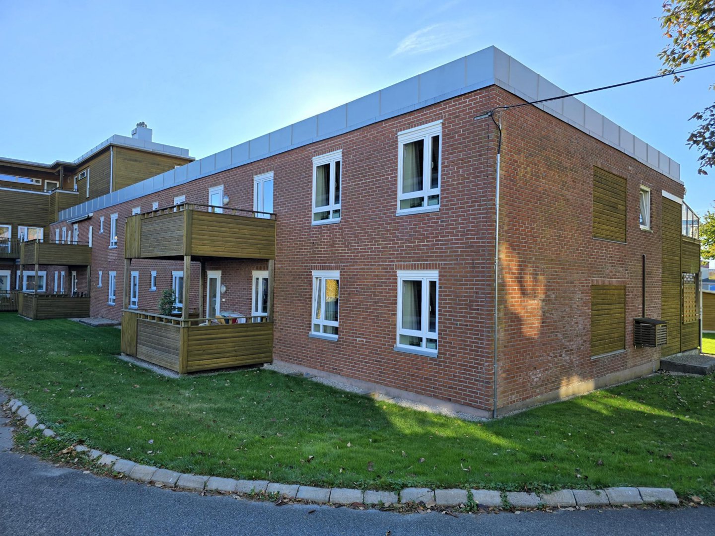 Fotografi av en eksisterende eller ferdigbygd leilighetsbygning med røde teglvegger, hvite vinduer og trebalconier.