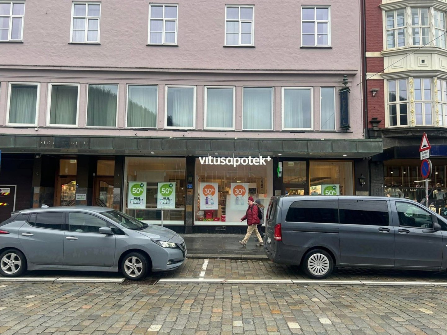 Fotografi av en fasade på et apotek (Vitusapotek) med parkerte biler foran.