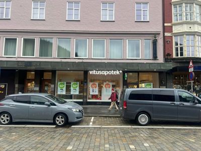 Fotografi av en fasade på et apotek (Vitusapotek) med parkerte biler foran.