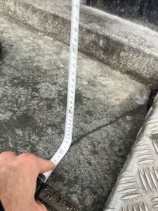 Fotografi av en hånd som holder en målebånd over en betongtrapp for å måle høyden på trinnene.