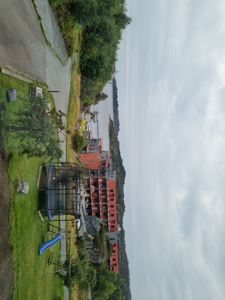 Fotografi av en bygning (muligens et barnehage- eller skolebygg) sett fra en høyde, med omgivelser som vei, grøntområde og vann i bakgrunnen.